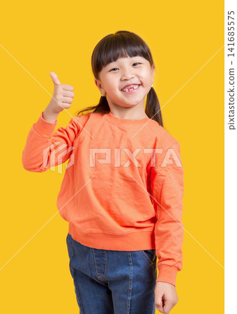 Happy Asian schoolgirl showing thumbs up, excited child on yellow background, approval and success concept Happy Asian schoolgirl showing thumbs up, excited child on yellow background, approval and success concept 141685575
