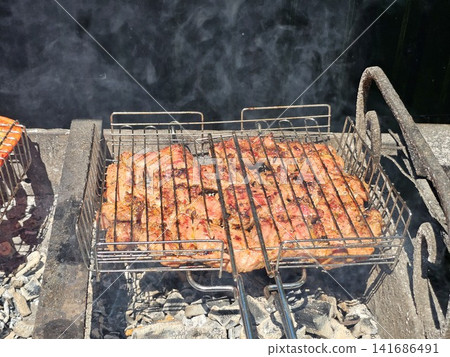 Juicy pork steaks grilling on metal barbecue grate over hot charcoal during sunny outdoor barbecue cooking Juicy pork steaks grilling on metal barbecue grate over hot charcoal during sunny outdoor barbecue cooking 141686491