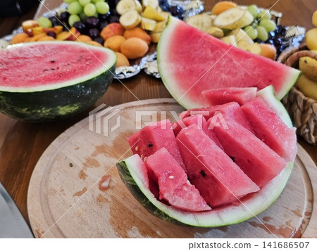 Watermelon slices arranged in rind like tree steps beside bananas and grapes, beautiful fruit serving on table, fresh summer food display 141686507