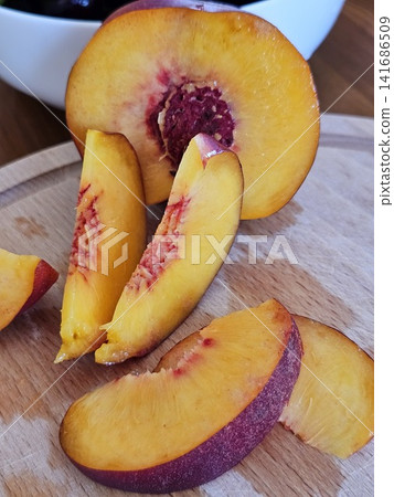 Fresh nectarine sliced into wedges on wooden cutting board by chef in black gloves for elegant serving, close up 141686509