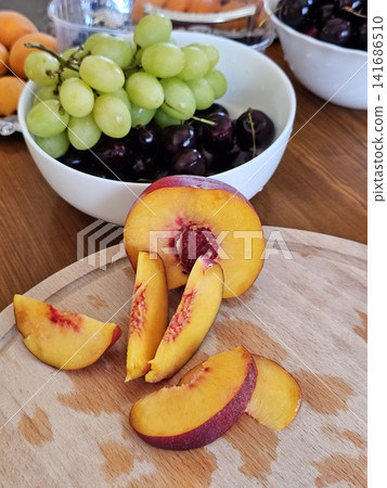 Fresh nectarine sliced into wedges on wooden cutting board by chef in black gloves for elegant serving, close up Fresh nectarine sliced into wedges on wooden cutting board by chef in black gloves for elegant serving, close up 141686510