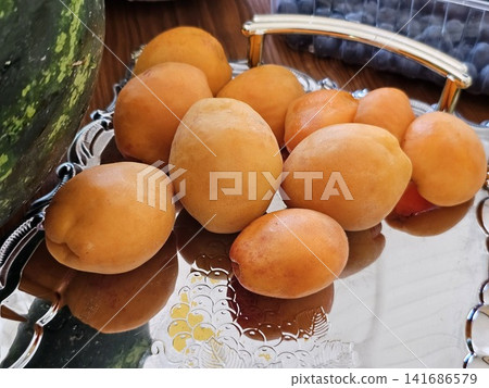 Apricot slices and whole apricots arranged on reflective glass mirror tray, elegant fresh fruit serving, colorful summer dessert presentation 141686579