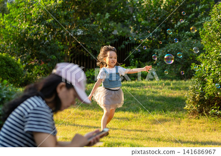 Little girl playing with bubbles in park while parent using smartphone, modern parenting and screen distraction concept Little girl playing with bubbles in park while parent using smartphone, modern parenting and screen distraction concept 141686967