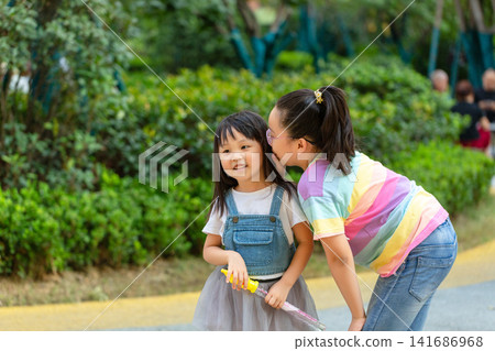 Two Asian Sisters Sharing a Secret Whispering in Park - Friendship and Sibling Bond Two Asian Sisters Sharing a Secret Whispering in Park - Friendship and Sibling Bond 141686968