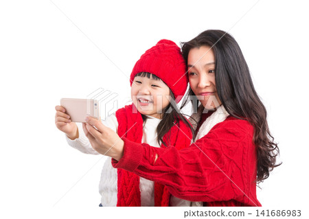 A mother and her young daughter holding a smartphone to take a selfie together. A mother and her young daughter holding a smartphone to take a selfie together. 141686983