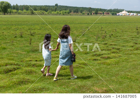 The backs of two Asian girls carrying DSLR cameras walking on the grassland The backs of two Asian girls carrying DSLR cameras walking on the grassland 141687005