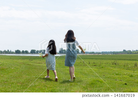A back view of two people walking together towards a lake in a green field. A back view of two people walking together towards a lake in a green field. 141687019