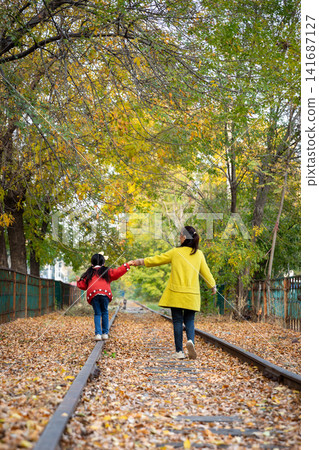 Asian mother and daughter walking on railway track in autumn park, warm emotion, family bonding and childhood care concept 141687127