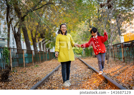 Asian mother and daughter walking on railway track in autumn park, warm emotion, family bonding and childhood care concept Asian mother and daughter walking on railway track in autumn park, warm emotion, family bonding and childhood care concept 141687129