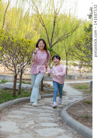 A woman and a young girl holding hands while running down a stone pathway. A woman and a young girl holding hands while running down a stone pathway. 141687132