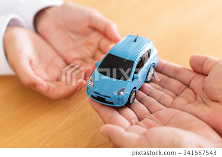 The hands of a man and a woman handing over a model car. The hands of a man and a woman handing over a model car. 141687543