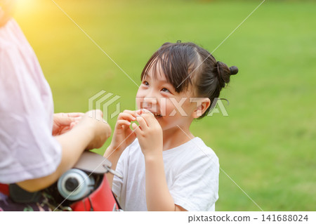 Cute little girl looking at mother asking for snacks or sweets with happy smile in park Cute little girl looking at mother asking for snacks or sweets with happy smile in park 141688024