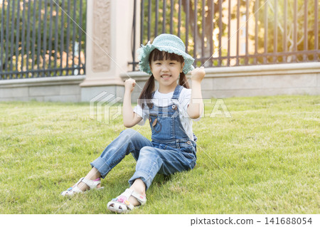 Happy Asian Little Girl Playing on Green Grass in Summer Park Happy Asian Little Girl Playing on Green Grass in Summer Park 141688054