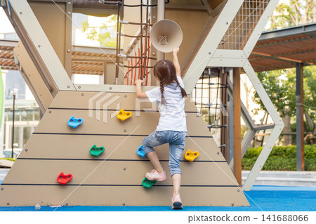 Back view of a brave young girl reaching for the top of a modern climbing frame at a neighborhood park. Back view of a brave young girl reaching for the top of a modern climbing frame at a neighborhood park. 141688066