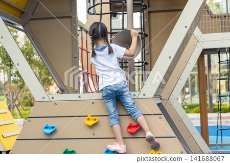 Back view of a brave young girl reaching for the top of a modern climbing frame at a neighborhood park. Back view of a brave young girl reaching for the top of a modern climbing frame at a neighborhood park. 141688067
