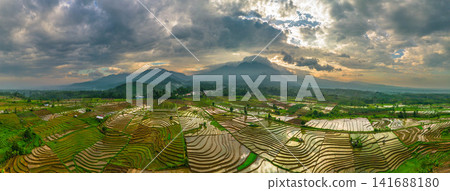 Aerial view of Sapa rice terraces at sunrise with golden light over green fields and misty mountain valleys Aerial view of Sapa rice terraces at sunrise with golden light over green fields and misty mountain valleys 141688180