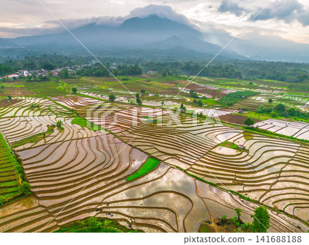 Aerial view of Sapa rice terraces at sunrise with golden light over green fields and misty mountain valleys Aerial view of Sapa rice terraces at sunrise with golden light over green fields and misty mountain valleys 141688188