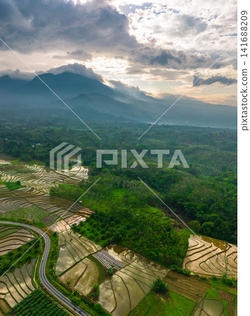 Aerial view of Sapa rice terraces at sunrise with golden light over green fields and misty mountain valleys Aerial view of Sapa rice terraces at sunrise with golden light over green fields and misty mountain valleys 141688209