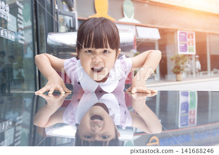 Energetic young girl shouting with an excited and playful expression while leaning on a glossy surface. Energetic young girl shouting with an excited and playful expression while leaning on a glossy surface. 141688246
