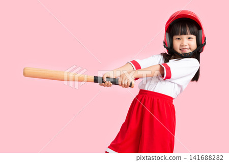 Close up of a smiling young girl in a red helmet practicing her baseball swing in studio. Close up of a smiling young girl in a red helmet practicing her baseball swing in studio. 141688282