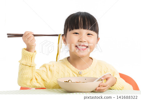 Happy Asian Little Girl Eating Noodles with Chopsticks at Dining Table Isolated on White Background Happy Asian Little Girl Eating Noodles with Chopsticks at Dining Table Isolated on White Background 141688322