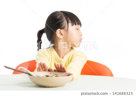 Asian Little Girl Refusing to Eat at Dining Table with Unhappy Expression Isolated on White Background 141688323