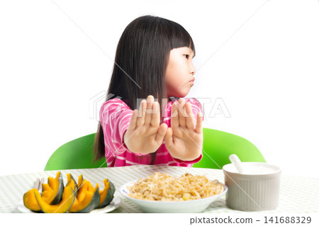 Asian Little Girl Refusing to Eat at Dining Table with Unhappy Expression Isolated on White Background Asian Little Girl Refusing to Eat at Dining Table with Unhappy Expression Isolated on White Background 141688329
