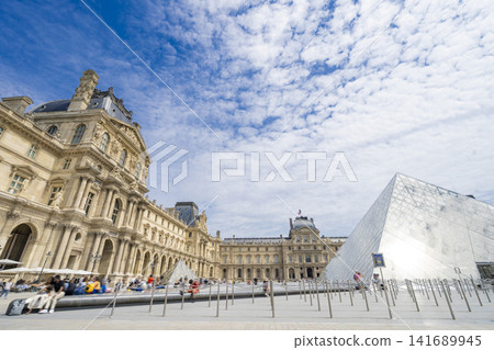 The Louvre Museum and the glass pyramid against a backdrop of blue skies and clouds. 141689945