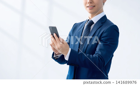拿著智慧型手機的微笑的男性商人 拿著智慧型手機的微笑的男性商人 141689976