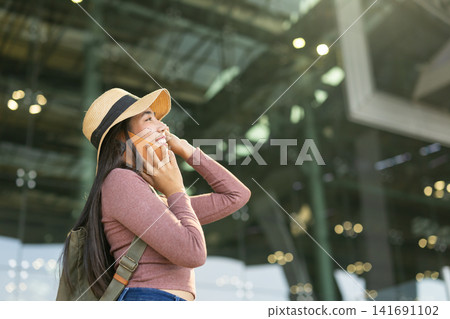 Happy Asian woman tourist smile with phone calling, Backpack female traveler enjoy journey trip tour standing against airport building facade with smartphone Happy Asian woman tourist smile with phone calling, Backpack female traveler enjoy journey trip tour standing against airport building facade with smartphone 141691102