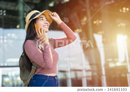 Happy Asian woman tourist smile with phone calling, Backpack female traveler enjoy journey trip tour standing against airport building facade with smartphone Happy Asian woman tourist smile with phone calling, Backpack female traveler enjoy journey trip tour standing against airport building facade with smartphone 141691103
