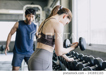 Healthy strong woman lifting high weight dumbbell a man looking amaze shock exciting pose 141691183