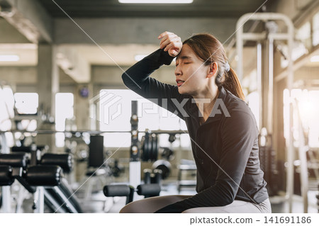 Sport woman tired exhausted fatigue sweating in sport fitness gym impact from heatwave hot condition Sport woman tired exhausted fatigue sweating in sport fitness gym impact from heatwave hot condition 141691186