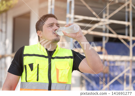 Outdoors worker impact from Heatwave in Europe, Engineer male construction builder drinking water Outdoors worker impact from Heatwave in Europe, Engineer male construction builder drinking water 141691277