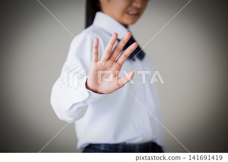A middle school girl in a uniform makes a gesture of refusal - gray background A middle school girl in a uniform makes a gesture of refusal - gray background 141691419