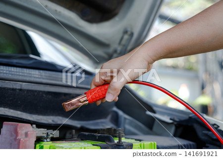 Hand holding jumper cable clamp near car battery Hand holding jumper cable clamp near car battery 141691921