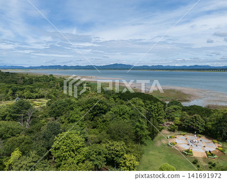 Drone aerial view of a large freshwater lake bordered by lush forest and distant mountains beneath expansive blue skies, showcasing natural landscape and tranquil scenery Drone aerial view of a large freshwater lake bordered by lush forest and distant mountains beneath expansive blue skies, showcasing natural landscape and tranquil scenery 141691972