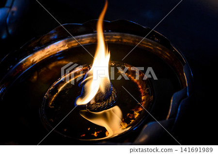 Close-up of a traditional oil lamp with a glowing flame in low light, symbolizing peace, spirituality, meditation, and hope Close-up of a traditional oil lamp with a glowing flame in low light, symbolizing peace, spirituality, meditation, and hope 141691989