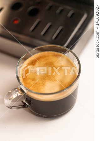 Close up of freshly brewed black coffee served in a clear glass cup with rich crema Close up of freshly brewed black coffee served in a clear glass cup with rich crema 141692027