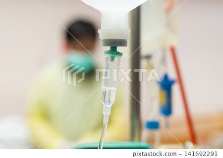 Intravenous drip delivering medical fluid hospital blurred healthcare worker background representing treatment recovery emergency care clinical support Intravenous drip delivering medical fluid hospital blurred healthcare worker background representing treatment recovery emergency care clinical support 141692291