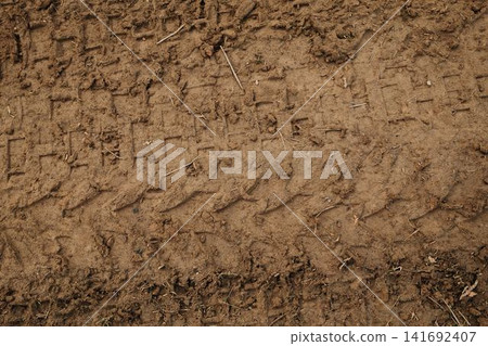 Close up of muddy ground with visible tire tread marks and soil texture. Abstract natural background with pattern and earth detail. Close up of muddy ground with visible tire tread marks and soil texture. Abstract natural background with pattern and earth detail. 141692407