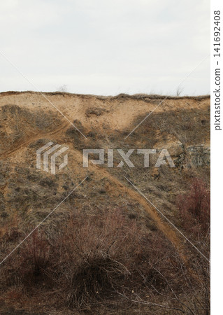 Steep sandy slope with narrow footpath and dry vegetation in Visnjicka Banja, Belgrade. Natural eroded hillside under overcast sky. Steep sandy slope with narrow footpath and dry vegetation in Visnjicka Banja, Belgrade. Natural eroded hillside under overcast sky. 141692408