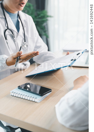 Doctor giving supportive medical advice to patient with clasped hands during clinic consultation, healthcare empathy, trust, comfort, treatment plan, and patient care concept. Doctor giving supportive medical advice to patient with clasped hands during clinic consultation, healthcare empathy, trust, comfort, treatment plan, and patient care concept. 141692448