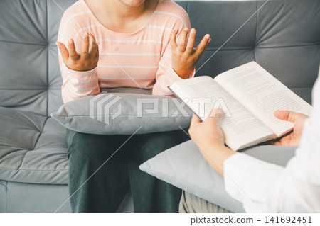 Female client explains feelings with open hands as therapist reads a book during counseling, showing talk therapy, emotional support, active listening, guidance, and mental wellness. Female client explains feelings with open hands as therapist reads a book during counseling, showing talk therapy, emotional support, active listening, guidance, and mental wellness. 141692451