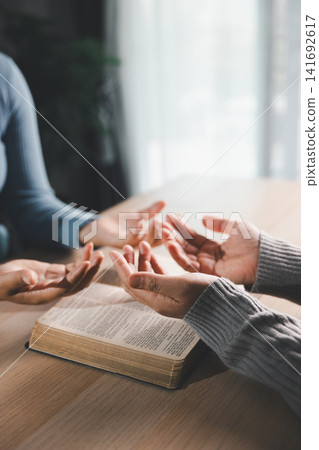 Group of people praying with open hands over an open Bible on a wooden table, Christian faith, worship, spiritual support, hope, and fellowship concept. Group of people praying with open hands over an open Bible on a wooden table, Christian faith, worship, spiritual support, hope, and fellowship concept. 141692617