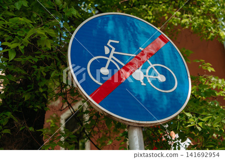 A blue bicycle road sign crossed with a red stripe marks the end of a cycling route. Traffic regulation, route change, transport policy, and urban navigation A blue bicycle road sign crossed with a red stripe marks the end of a cycling route. Traffic regulation, route change, transport policy, and urban navigation 141692954
