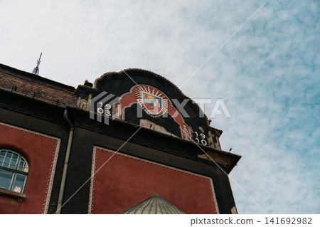 Ornamental facade detail of Subotica City Hall rises beneath a bright sky in Subotica, Serbia. Historic architecture, decorative design, and cultural heritage with elegant urban appeal Ornamental facade detail of Subotica City Hall rises beneath a bright sky in Subotica, Serbia. Historic architecture, decorative design, and cultural heritage with elegant urban appeal 141692982