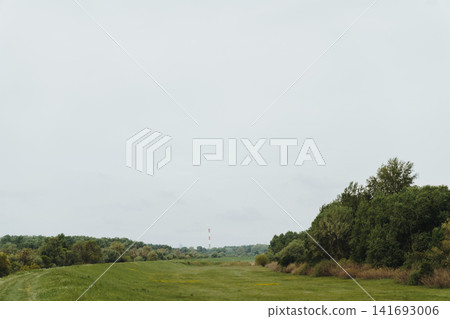 Open spring meadow with distant industrial chimney and tree line in the Belgrade suburb, Serbia. Concept of rural landscape, urban edge, and contrast between nature and industry Open spring meadow with distant industrial chimney and tree line in the Belgrade suburb, Serbia. Concept of rural landscape, urban edge, and contrast between nature and industry 141693006