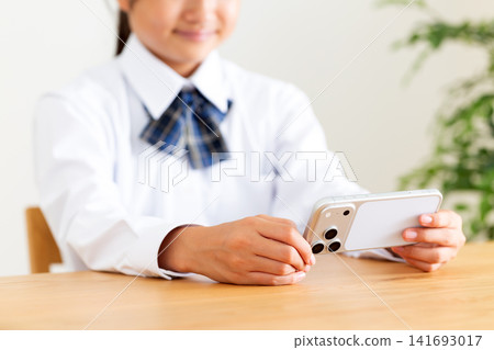 一名身穿校服的中學生正在客廳的桌子上看著她的智慧型手機。 141693017