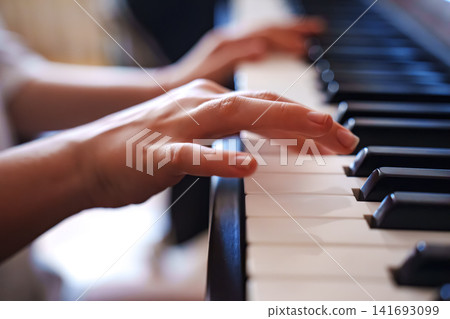Hands play piano keys in a light-filled room during afternoon Hands play piano keys in a light-filled room during afternoon 141693099